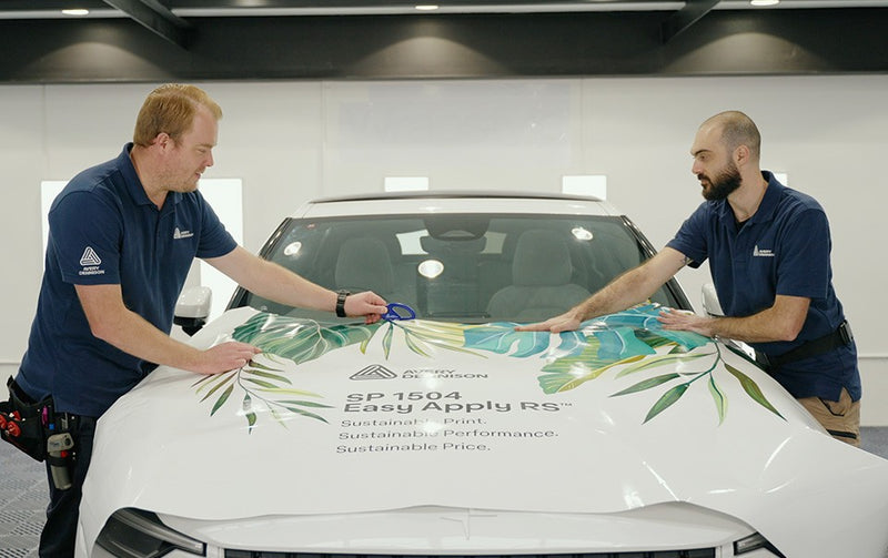 2 men are cutting and laying down the new SP1504 wrap onto a show vehicle, demonstrating the ease of application.